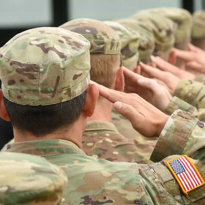 Saluting soldiers in camouflage uniform with American flag patch.